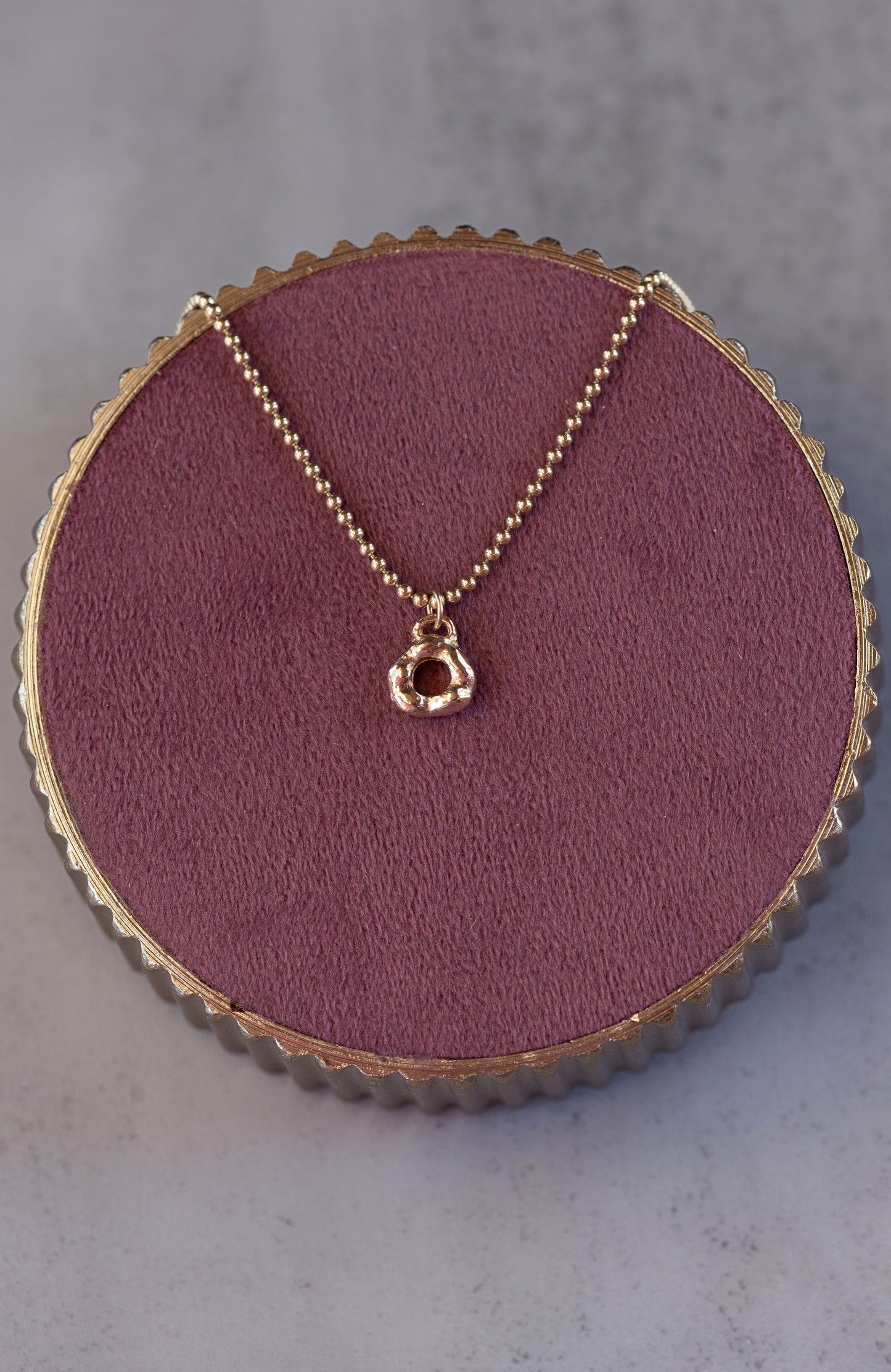 Gold necklace with a pendant on a round purple cushion against a gray background