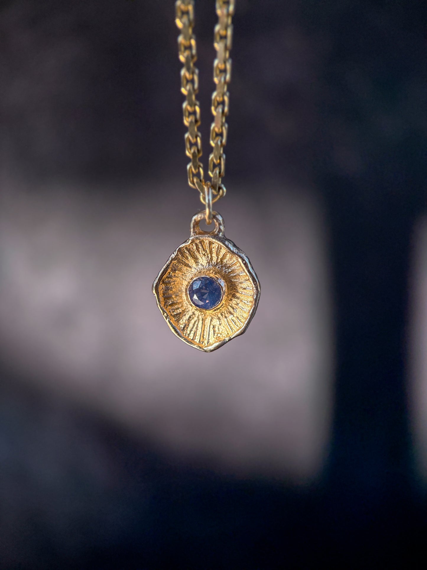 Gold necklace with a hexagonal pendant featuring a blue gemstone against a dark background