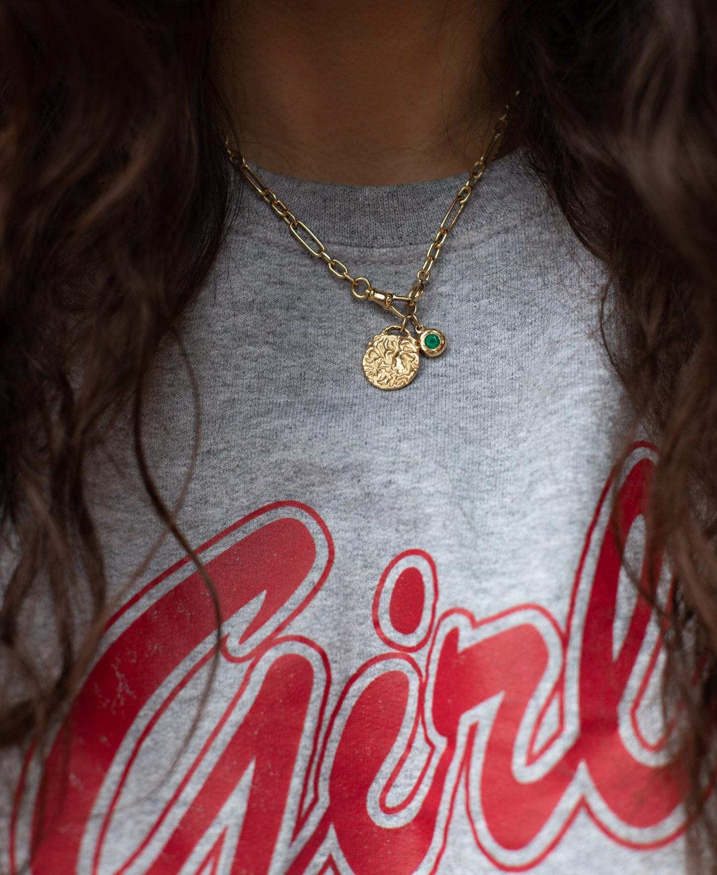 Person wearing a gold necklace with a pendant on a gray shirt with red text