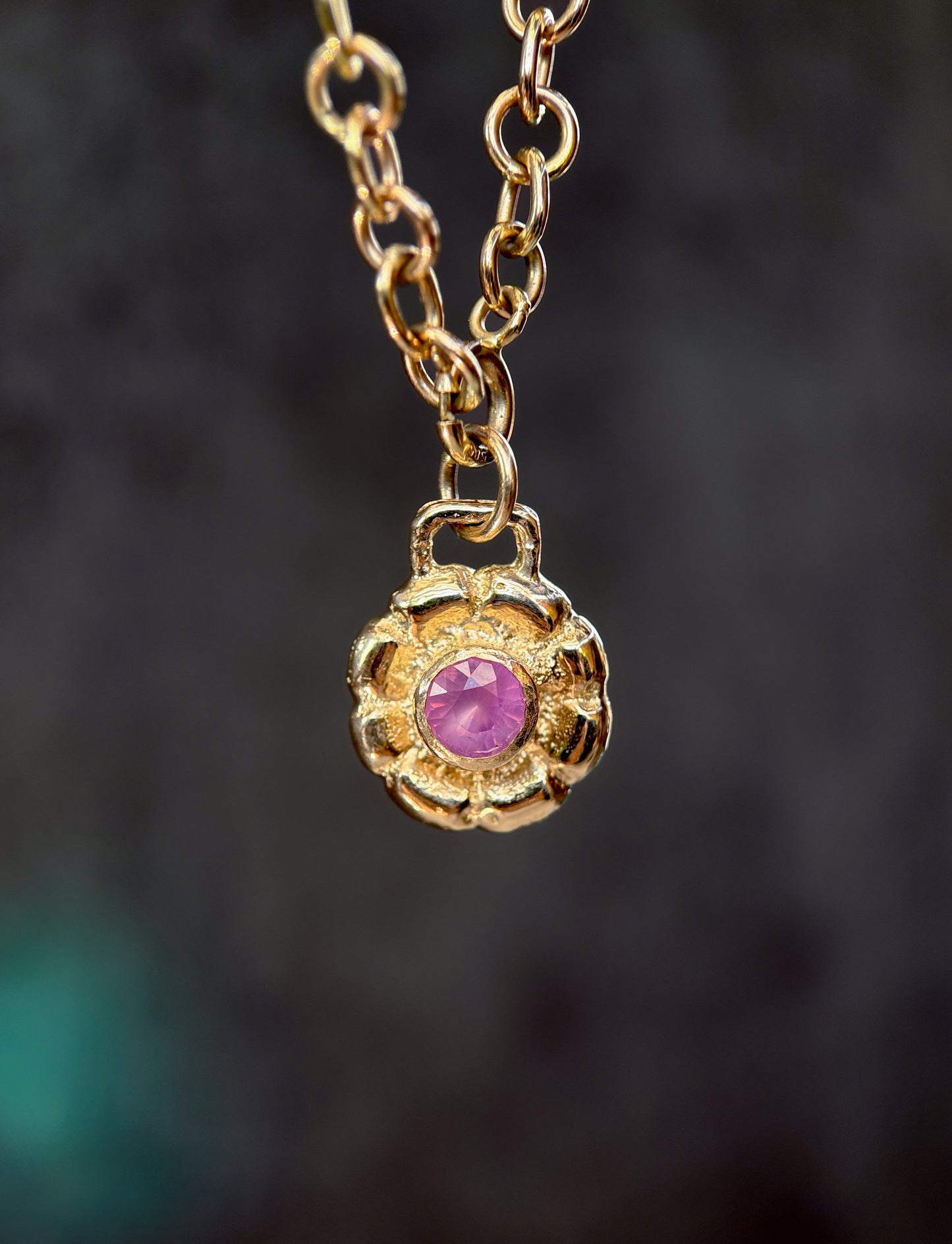 Gold necklace with a purple gemstone pendant on a dark background
