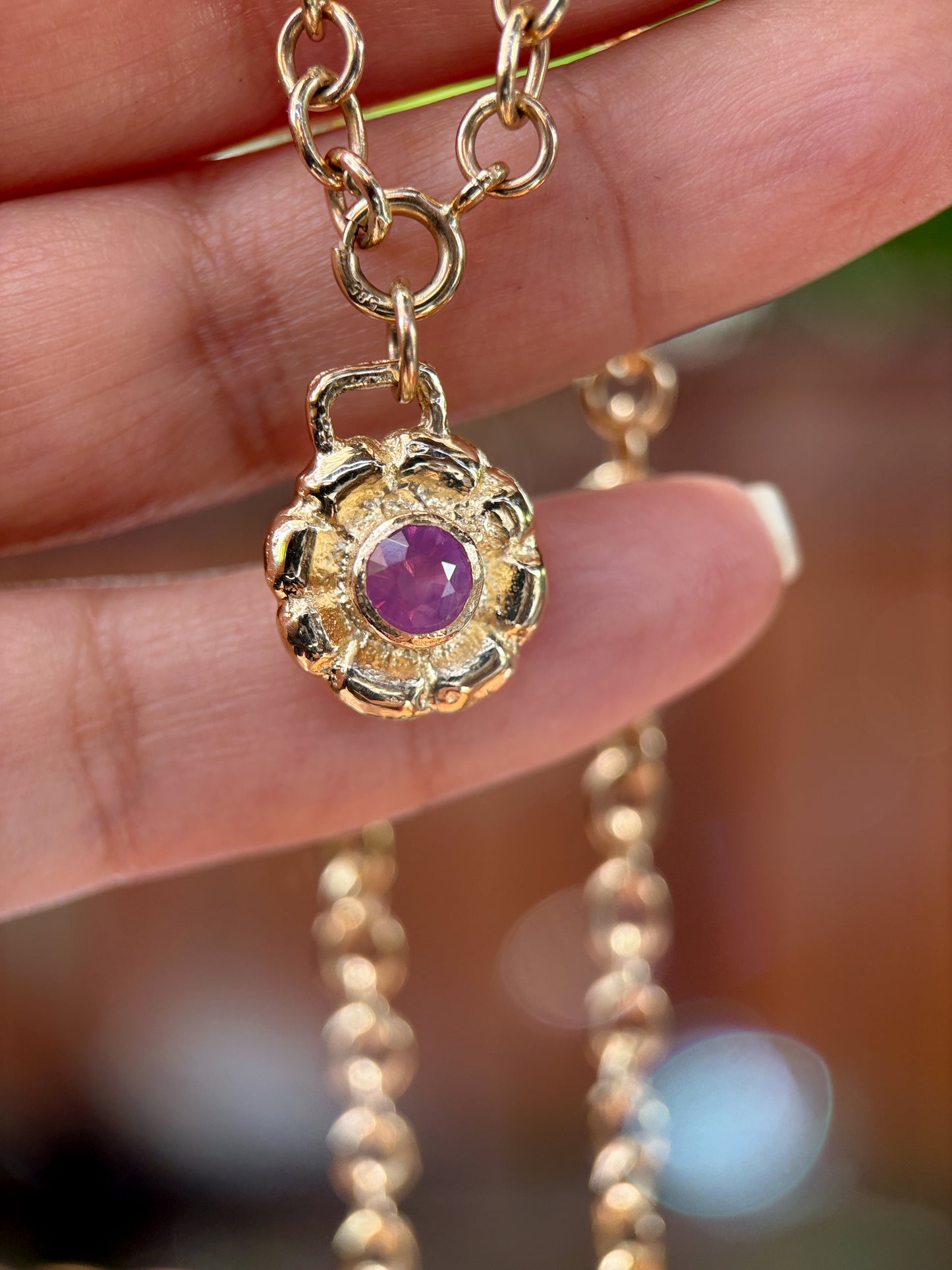 Gold necklace with a purple gemstone pendant held by a hand against a blurred background