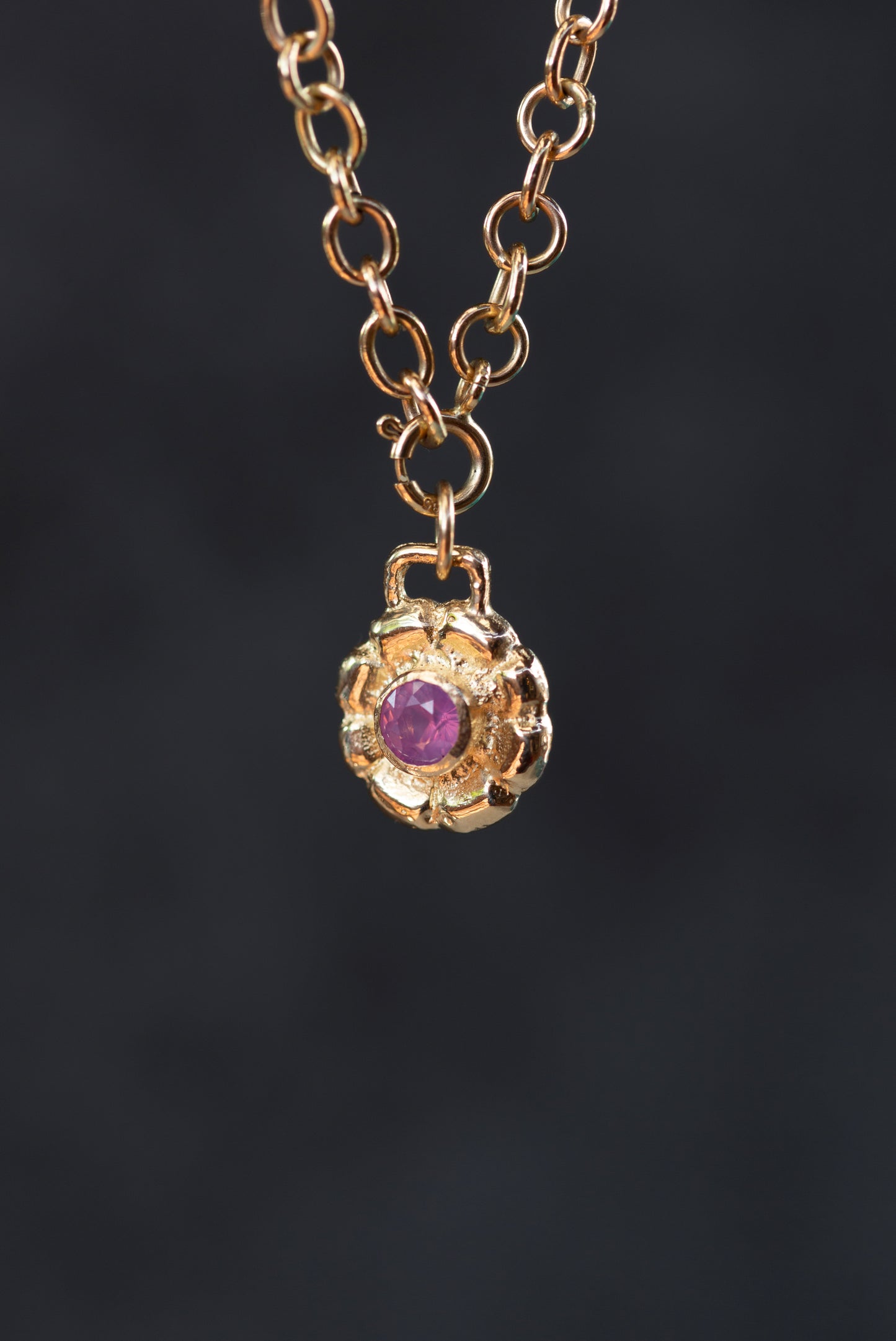 Gold necklace with a purple gemstone pendant on a dark background