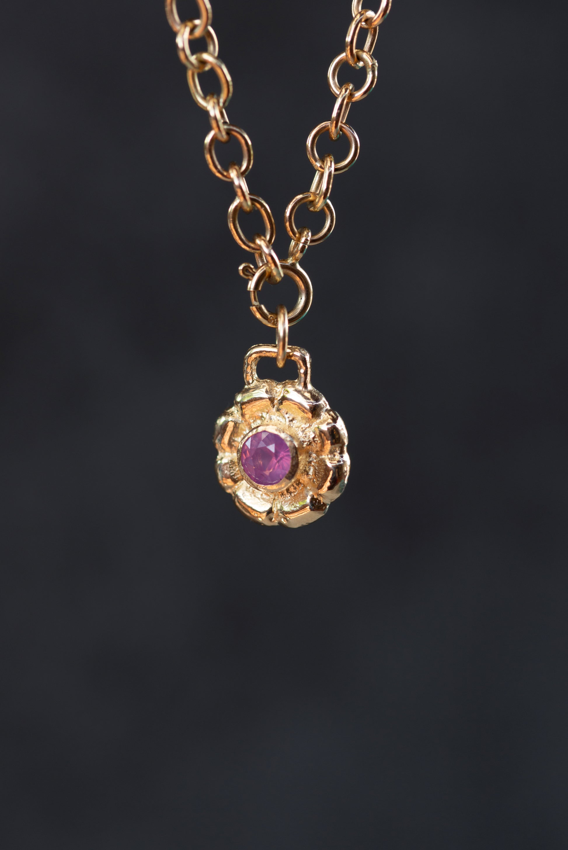 Gold necklace with a purple gemstone pendant on a dark background