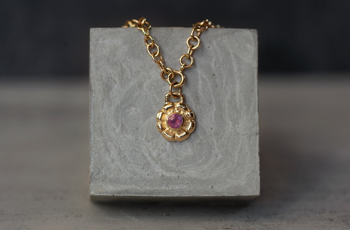 Gold necklace with a pink gemstone pendant on a gray stone surface