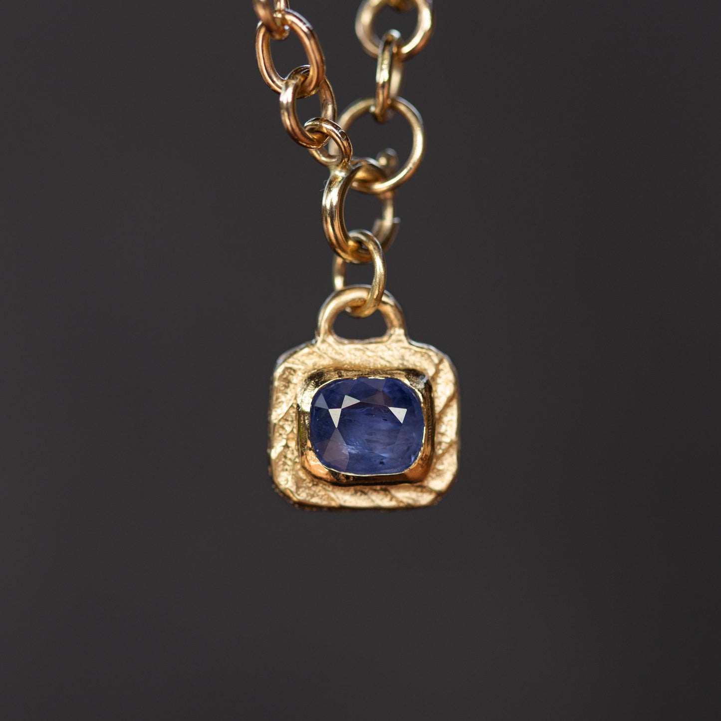 Gold necklace with a blue gemstone pendant on a dark background