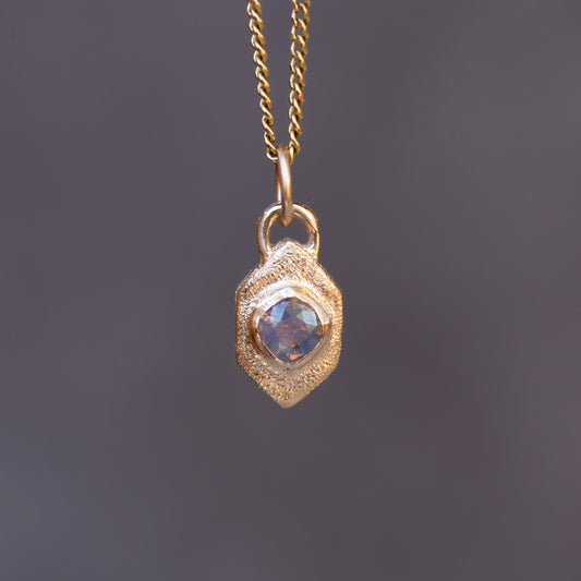 Gold necklace with a pendant featuring a blue gemstone on a dark gray background
