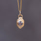 Gold necklace with a pendant featuring a blue gemstone on a dark gray background