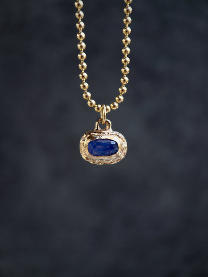 Gold necklace with a blue gemstone pendant on a dark background