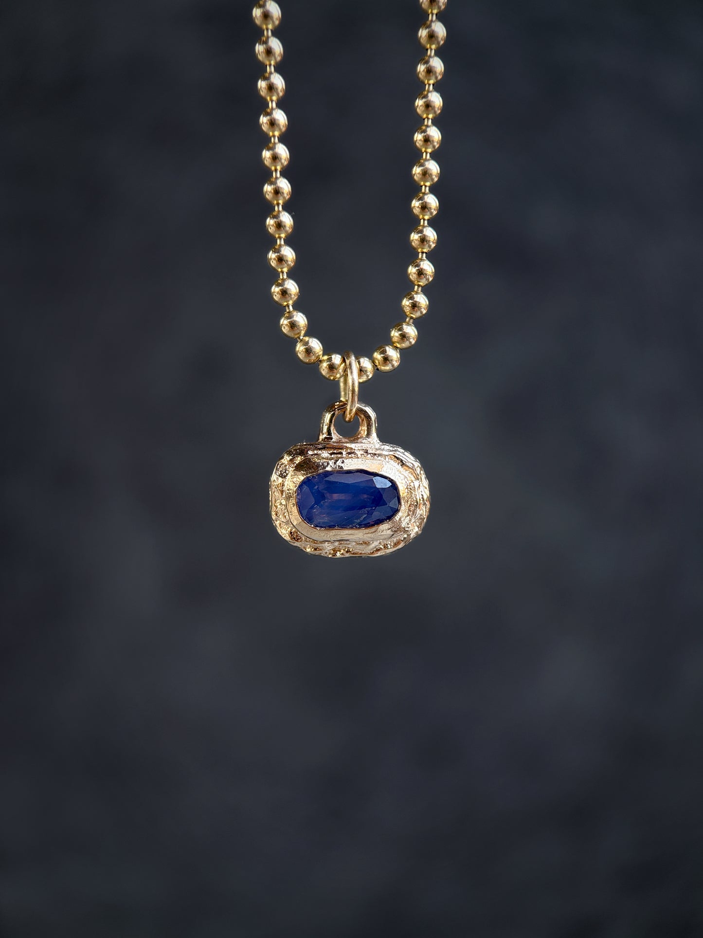 Gold necklace with a blue gemstone pendant on a dark background