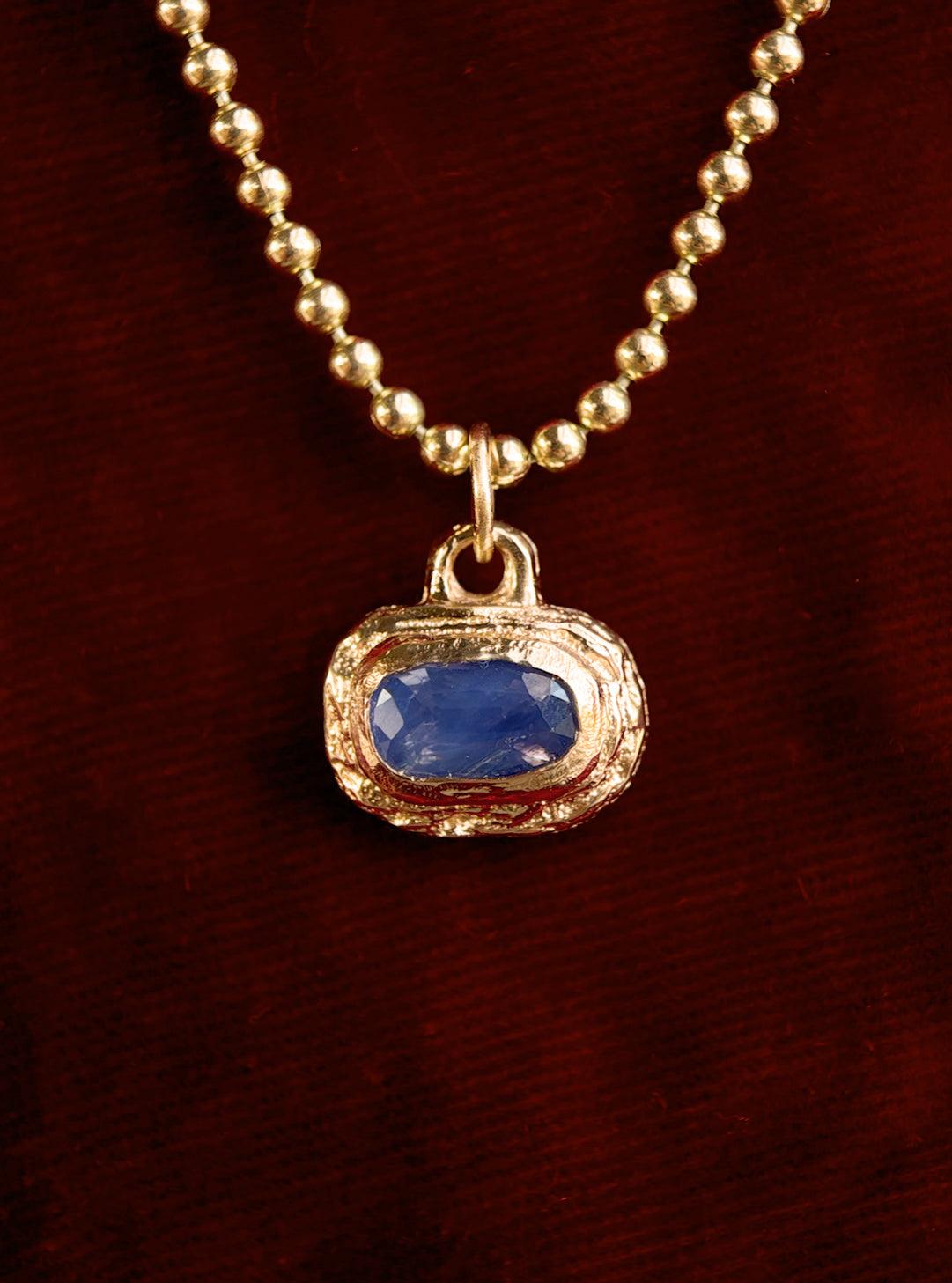 Gold necklace with a blue gemstone pendant on a dark red background