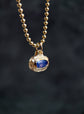 Gold necklace with a blue gemstone pendant on a dark background