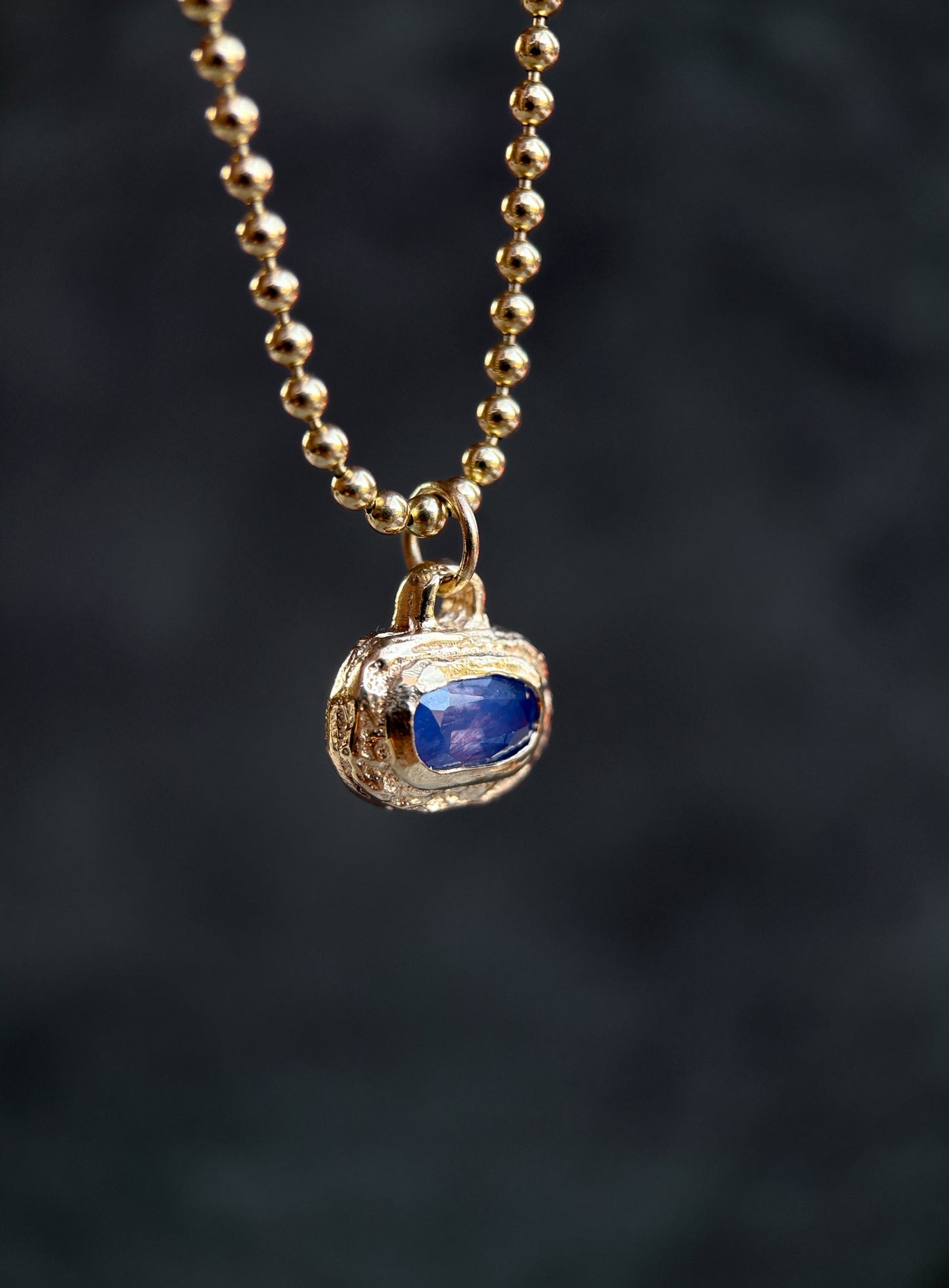 Gold necklace with a blue gemstone pendant on a dark background