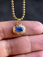 Gold necklace with a blue gemstone pendant held between fingers against a dark background