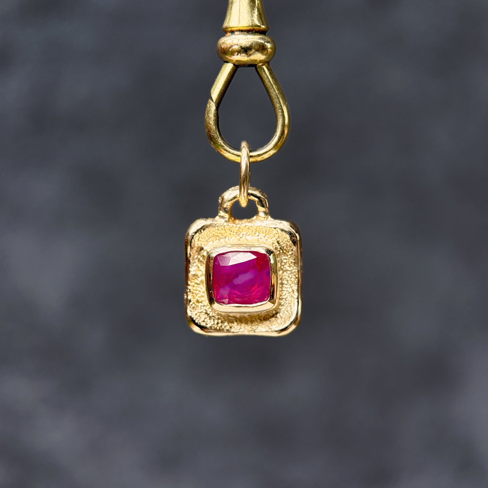 Gold pendant with a red gemstone on a dark gray background