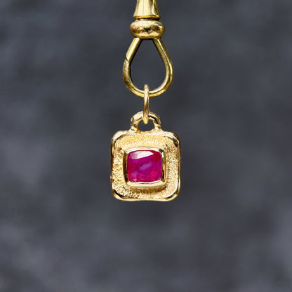 Gold pendant with a red gemstone on a dark gray background