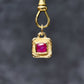 Gold pendant with a red gemstone on a dark gray background