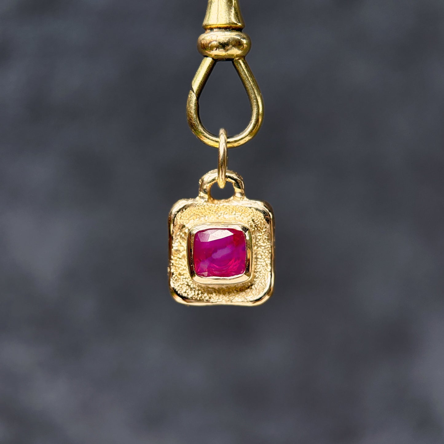 Gold pendant with a red gemstone on a dark gray background