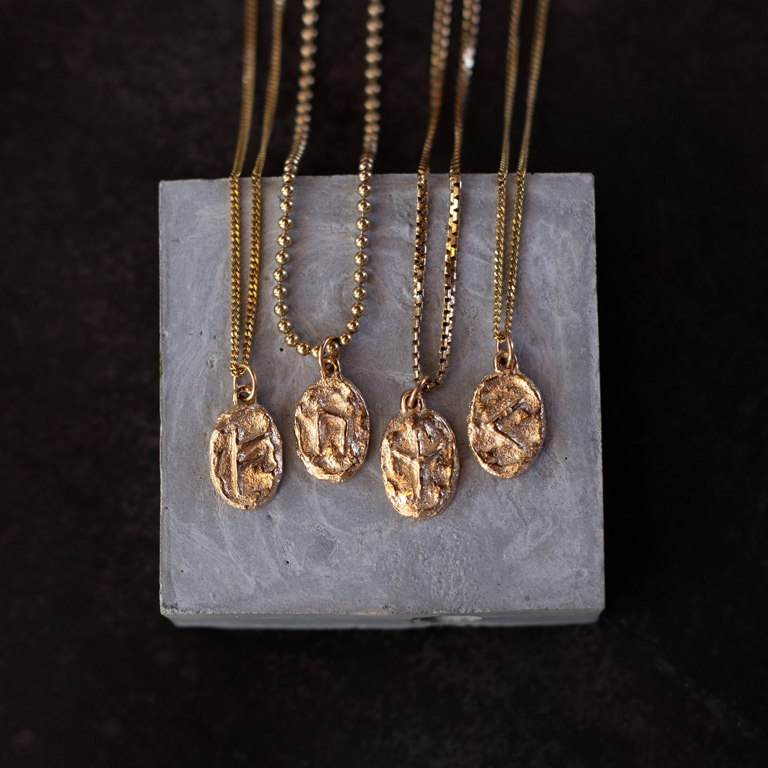 Gold necklaces with pendant designs on a gray stand against a dark background