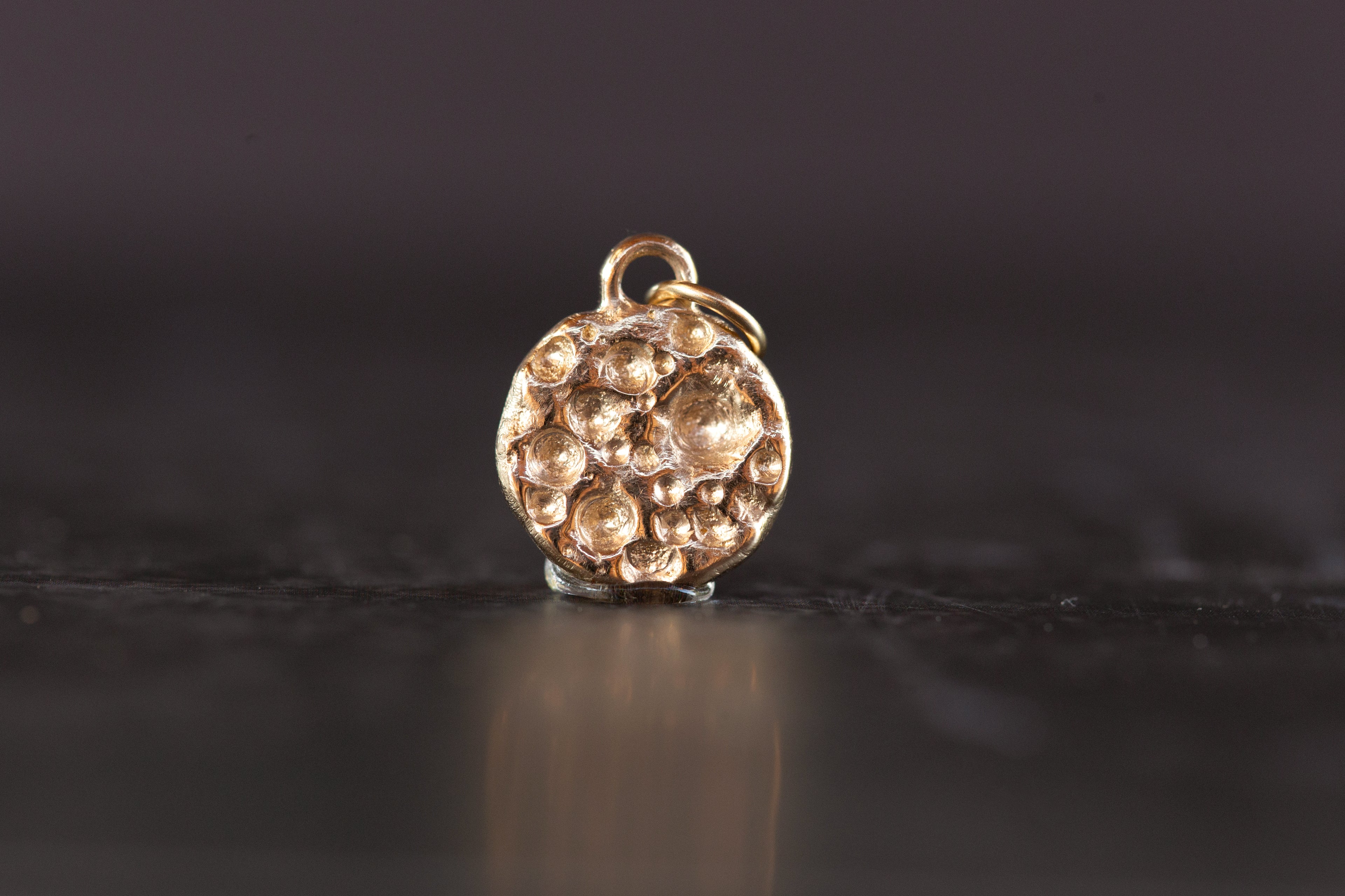 Gold textured charm on a dark reflective surface