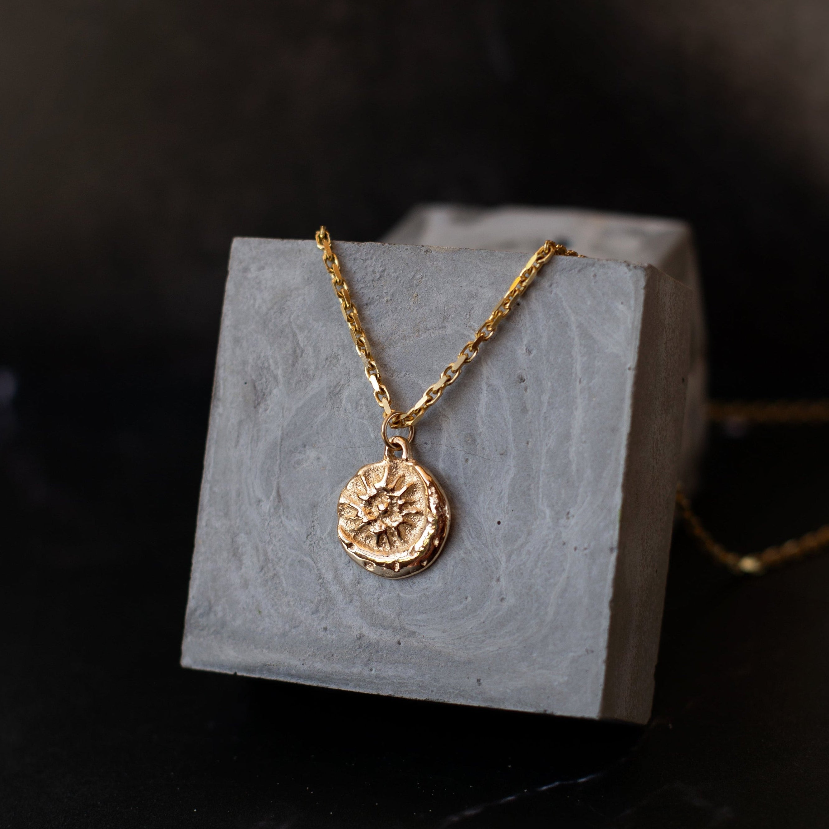 Gold necklace with a pendant on a gray stand against a dark background