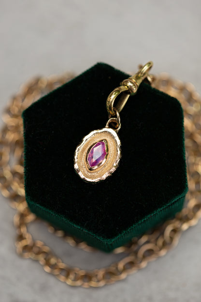 Gold necklace with a pendant featuring a pink gemstone on a green velvet stand.