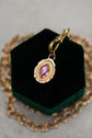 Gold necklace with a pendant featuring a pink gemstone on a green velvet stand.