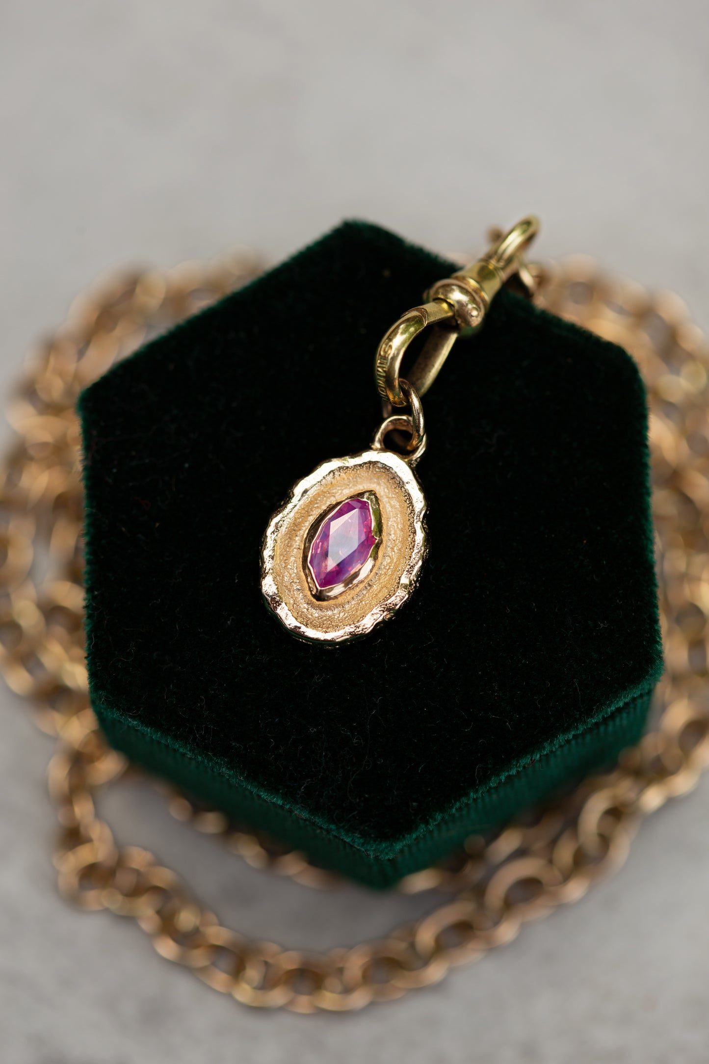 Gold necklace with a pendant featuring a pink gemstone on a green velvet stand.