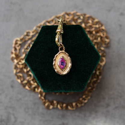 Gold pendant with a purple gemstone on a green velvet stand with a gold chain.
