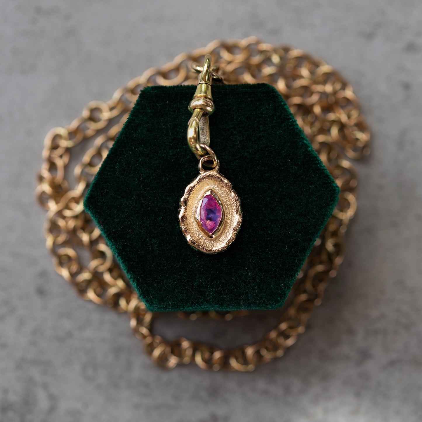 Gold pendant with a purple gemstone on a green velvet stand with a gold chain.