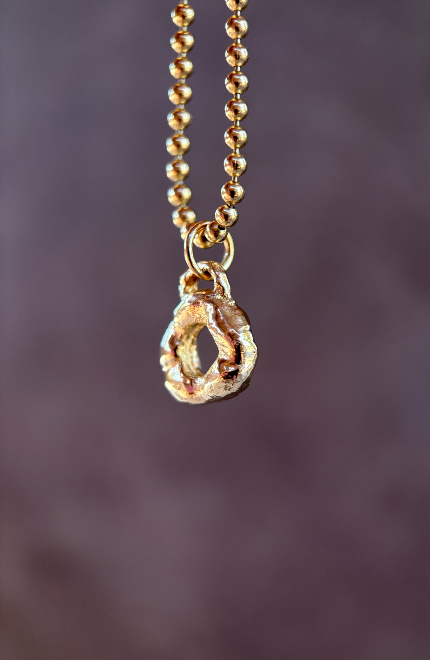 Gold necklace with a teardrop-shaped pendant on a blurred purple background