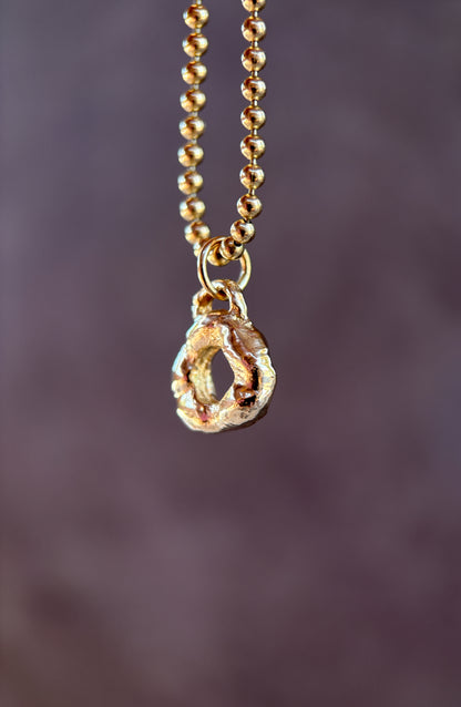 Gold necklace with a teardrop-shaped pendant on a blurred purple background
