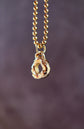 Gold necklace with a teardrop-shaped pendant on a blurred purple background
