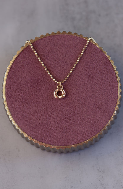 Gold necklace with a pendant on a round purple cushion against a gray background