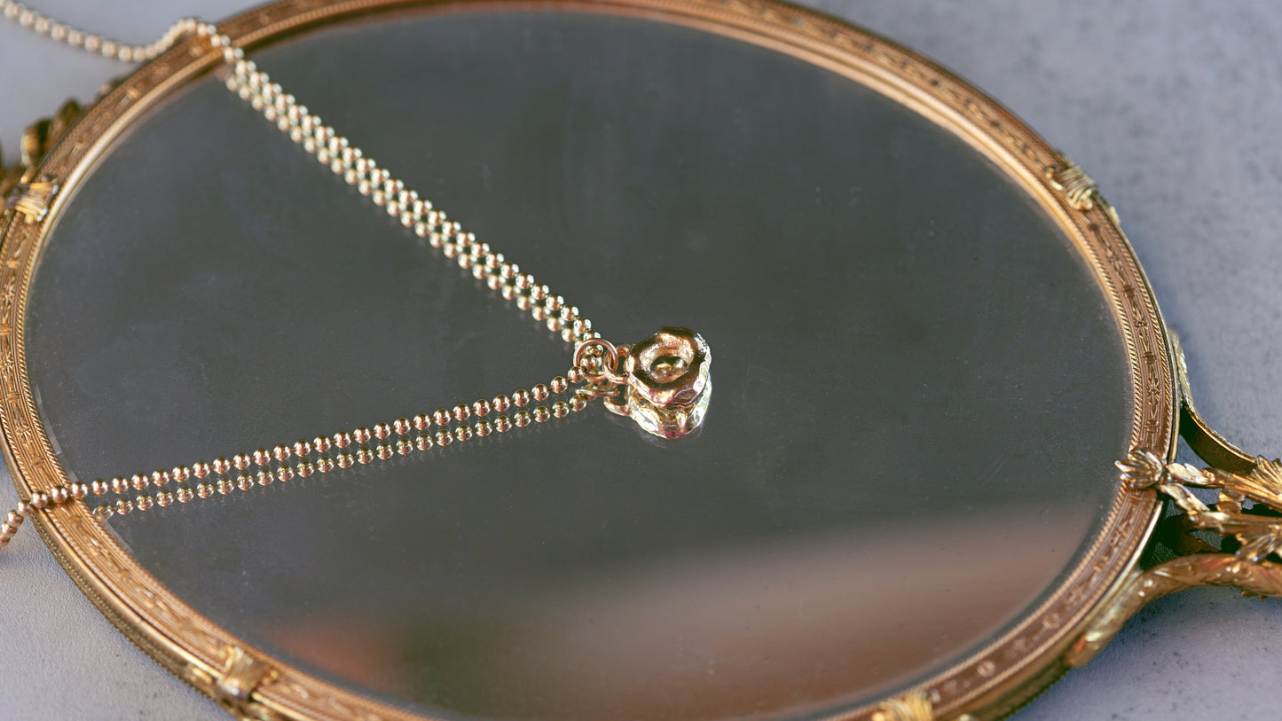 Gold necklace with a rose pendant on a round mirror with decorative frame