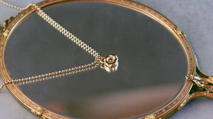 Gold necklace with a rose pendant on a round mirror with decorative frame