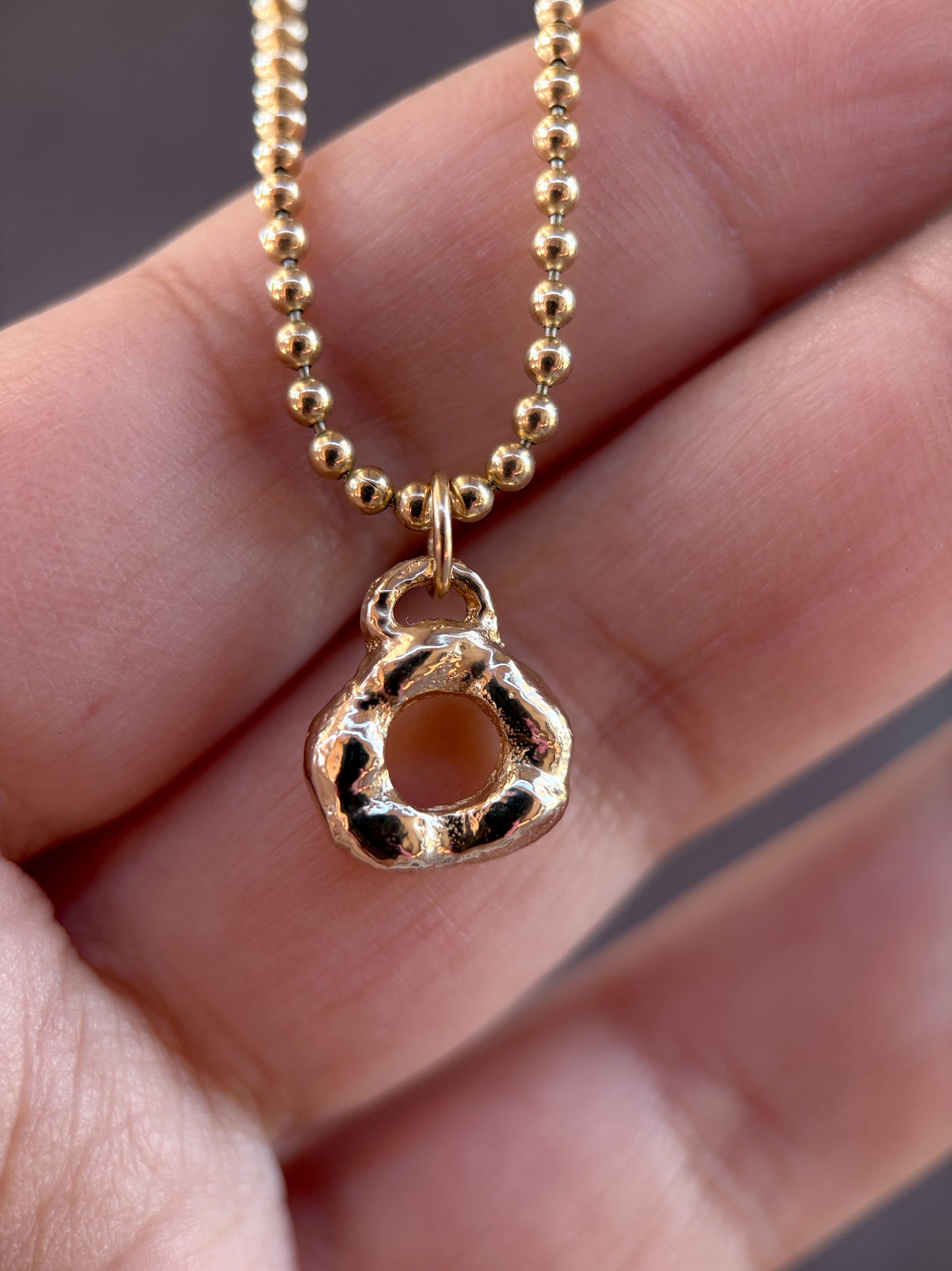 Gold necklace with a unique pendant held in a hand.