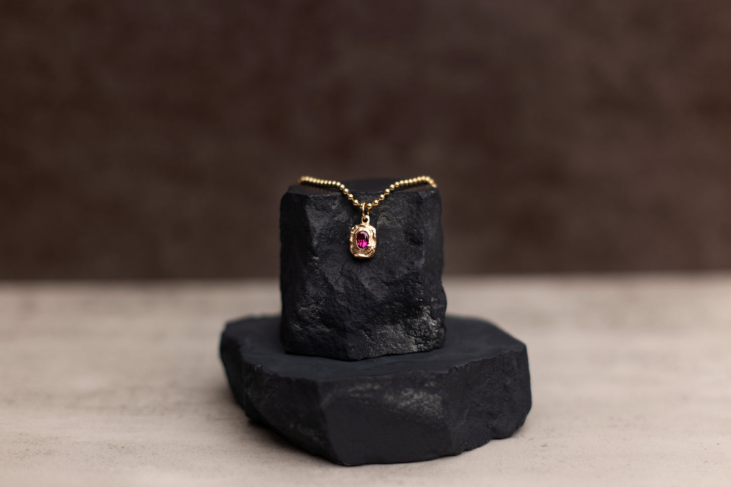 Gold necklace with a red gemstone pendant on a black stone stand against a dark background