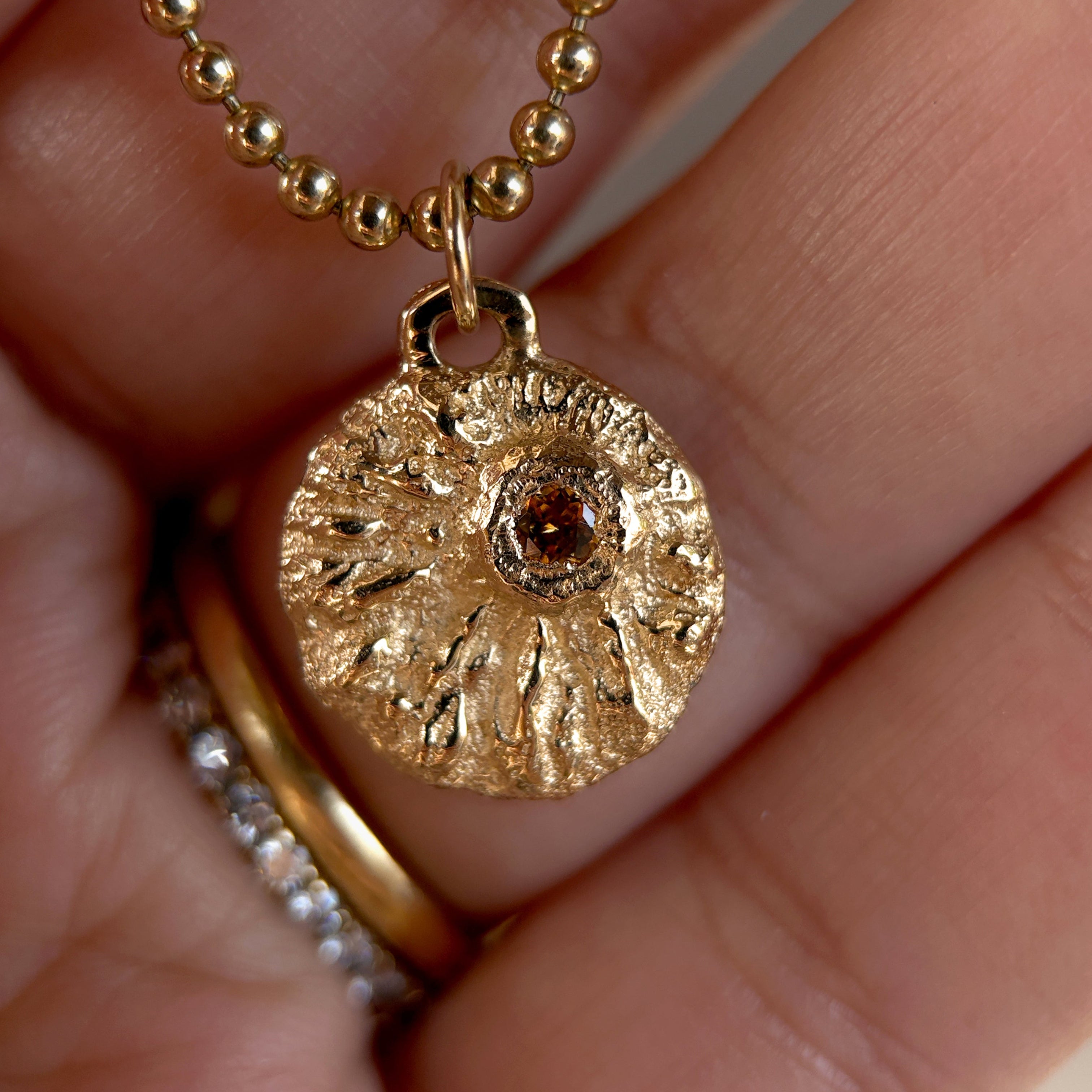 Gold necklace with a textured pendant held between fingers