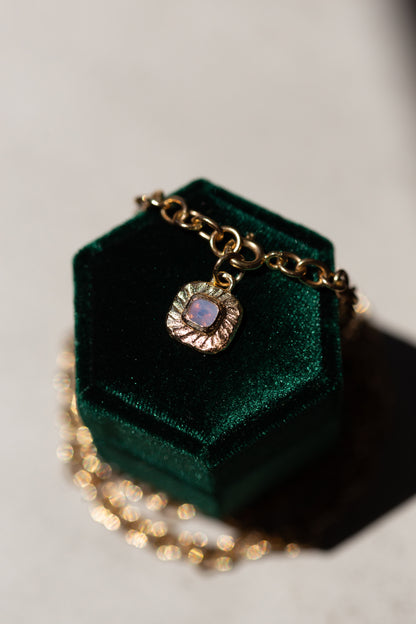 Gold necklace with a pendant on a green velvet box against a gray background