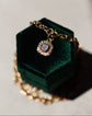 Gold necklace with a pendant on a green velvet box against a gray background