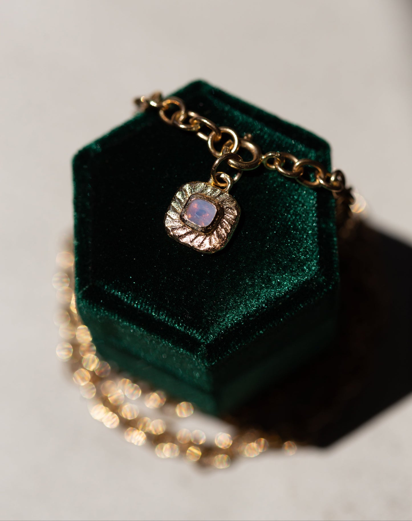 Gold necklace with a pendant on a green velvet box against a gray background