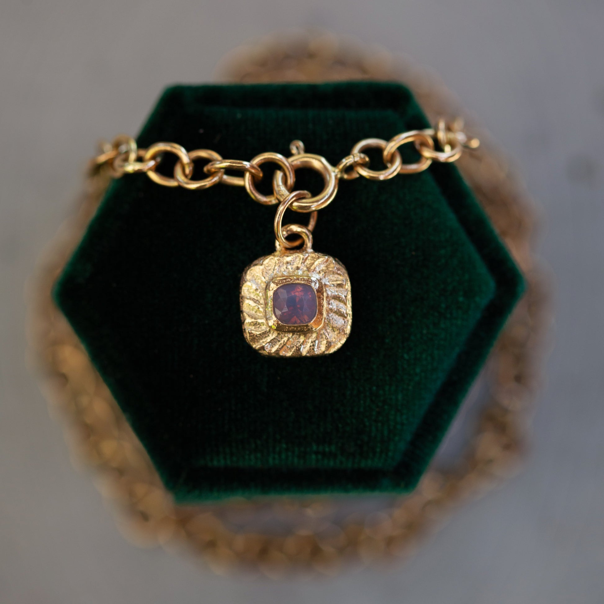 Gold bracelet with a purple gemstone charm on a green velvet stand.