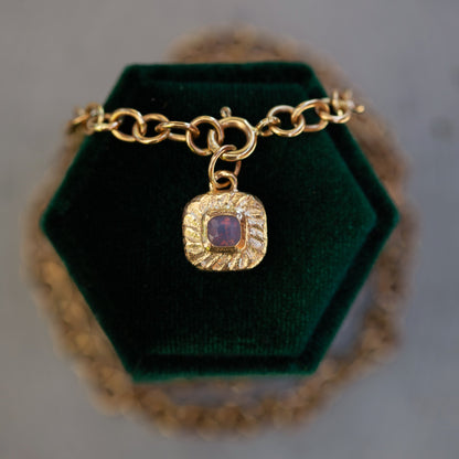 Gold bracelet with a purple gemstone charm on a green velvet stand.