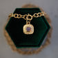 Gold bracelet with a purple gemstone charm on a green velvet stand.