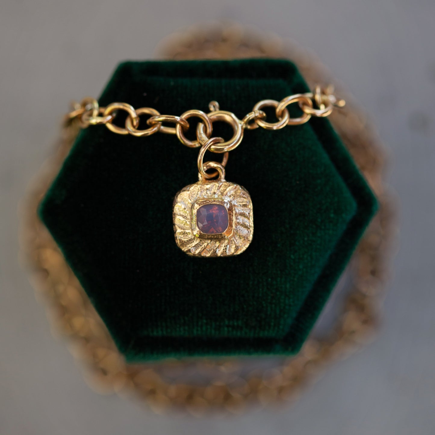 Gold bracelet with a purple gemstone charm on a green velvet stand.