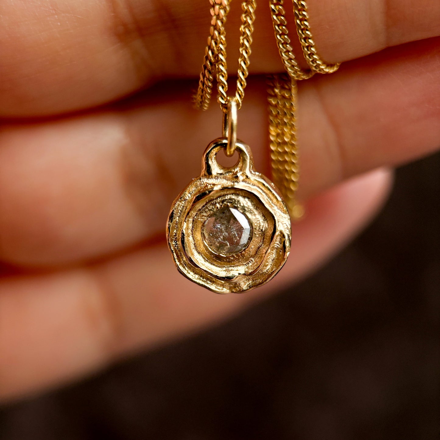 Gold necklace with a pendant featuring a diamond held by a hand against a blurred background