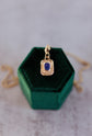 Gold pendant with a blue gemstone on a green velvet stand against a neutral background