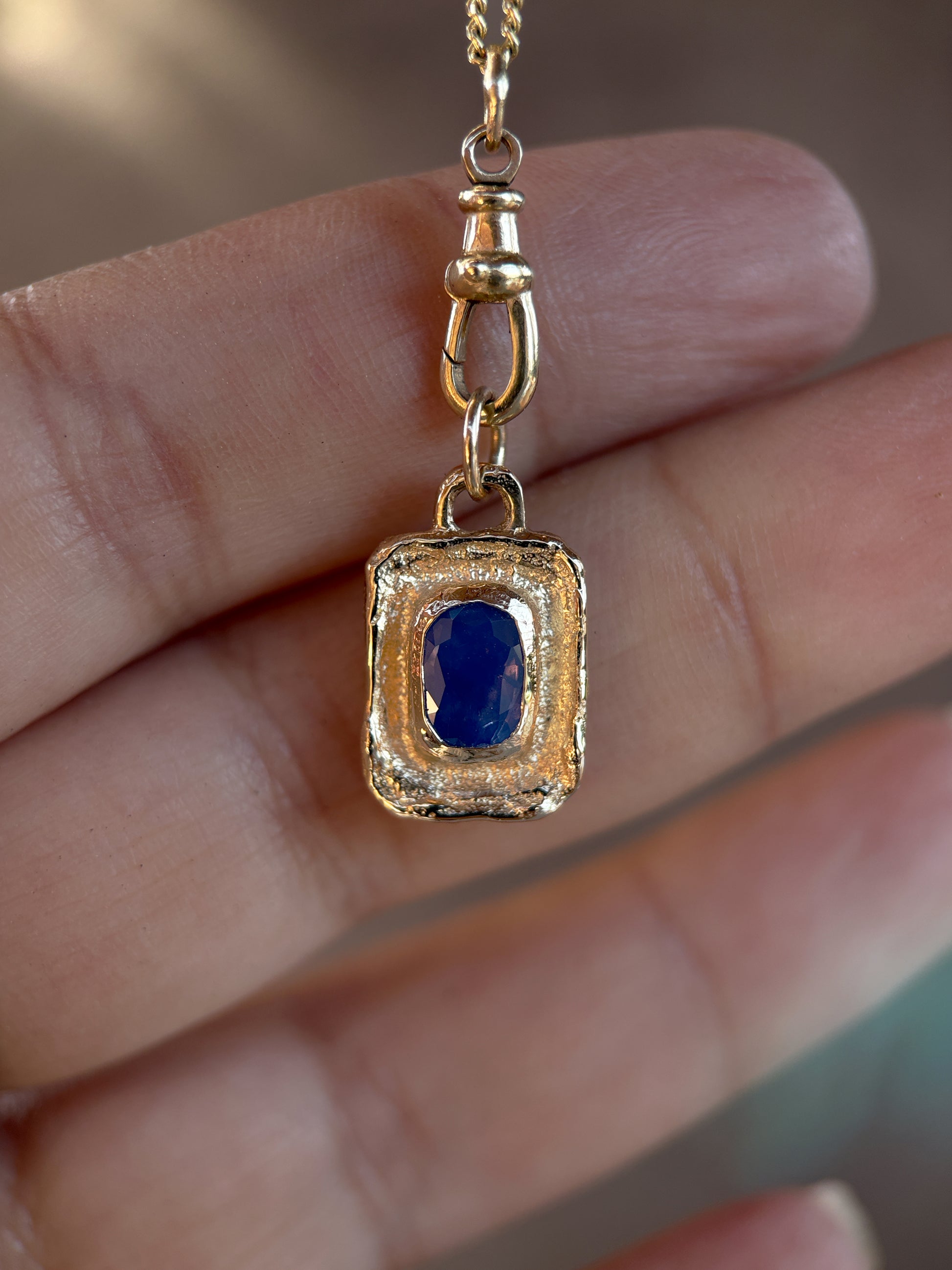 Gold pendant with a blue gemstone held between fingers