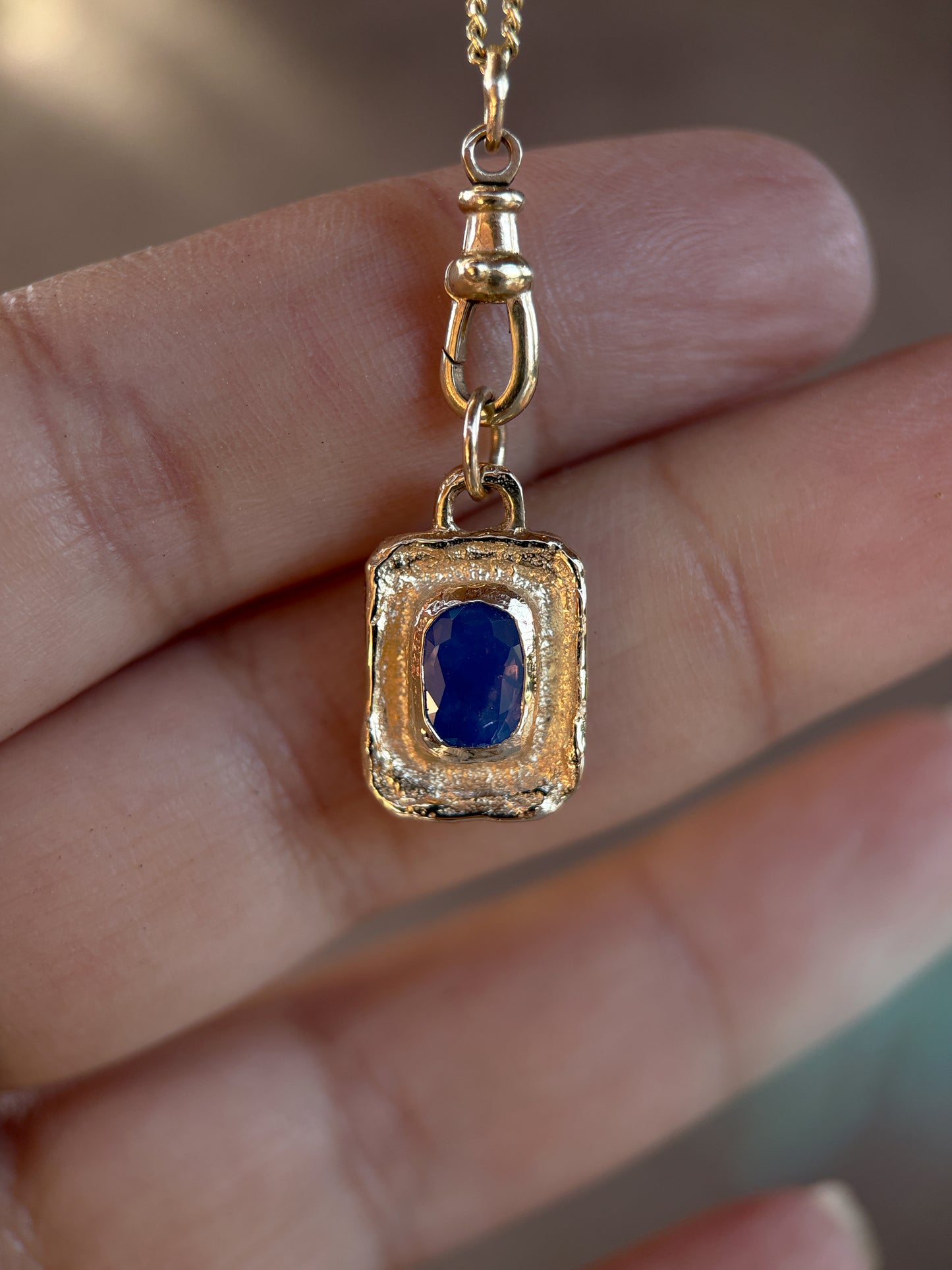 Gold pendant with a blue gemstone held between fingers