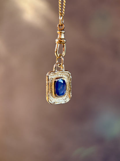 Gold pendant with a blue gemstone on a blurred background